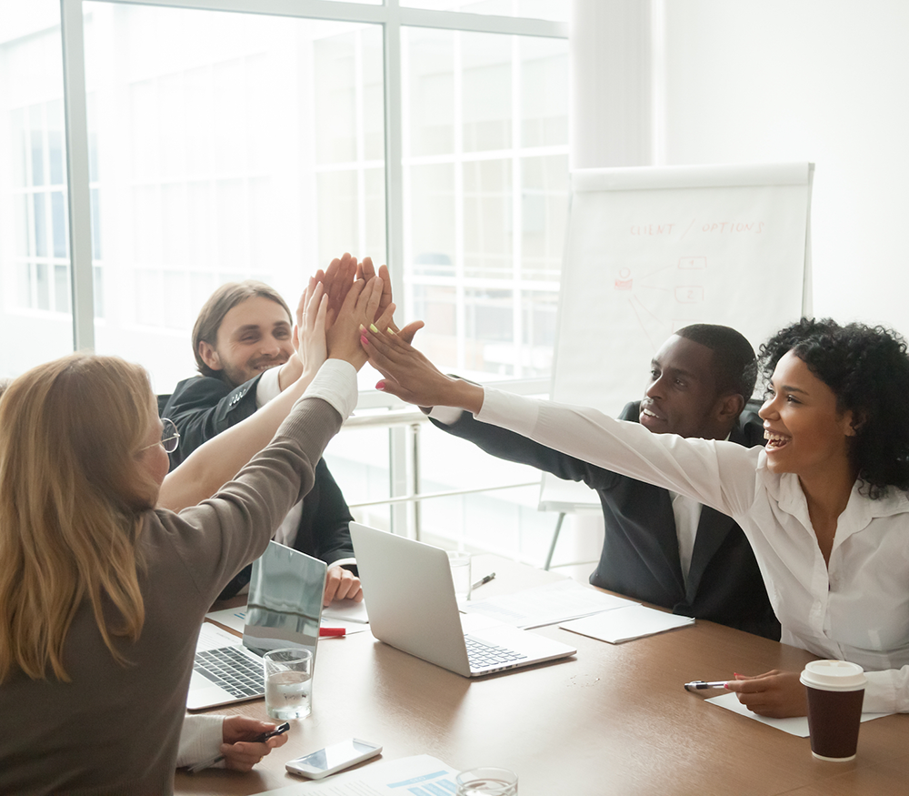 A group of colleagues high-fiving in a corporate board room for a grant application blog.